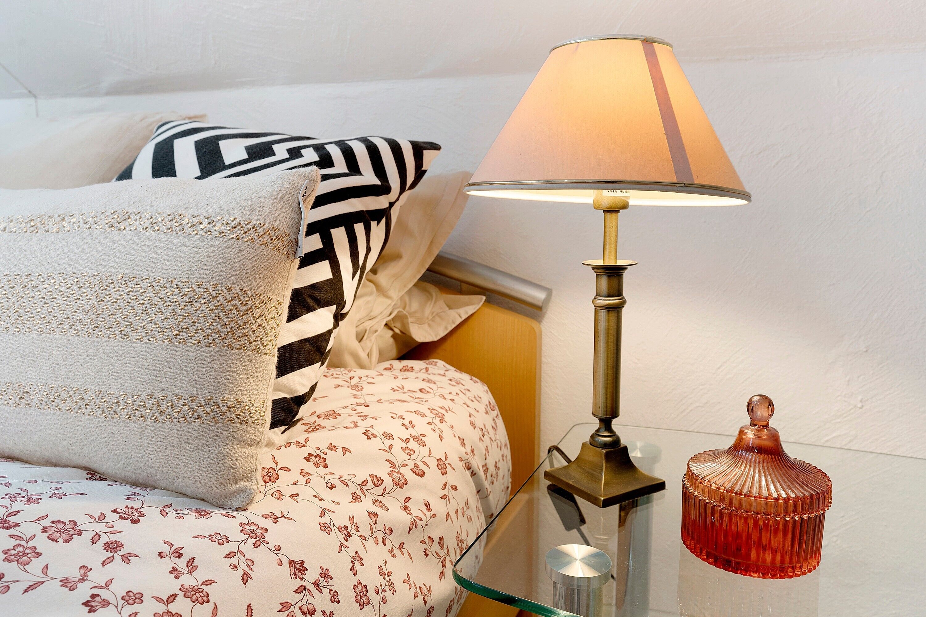 Un letto con biancheria a motivi, una lampada da comodino e un oggetto decorativo su un tavolino.