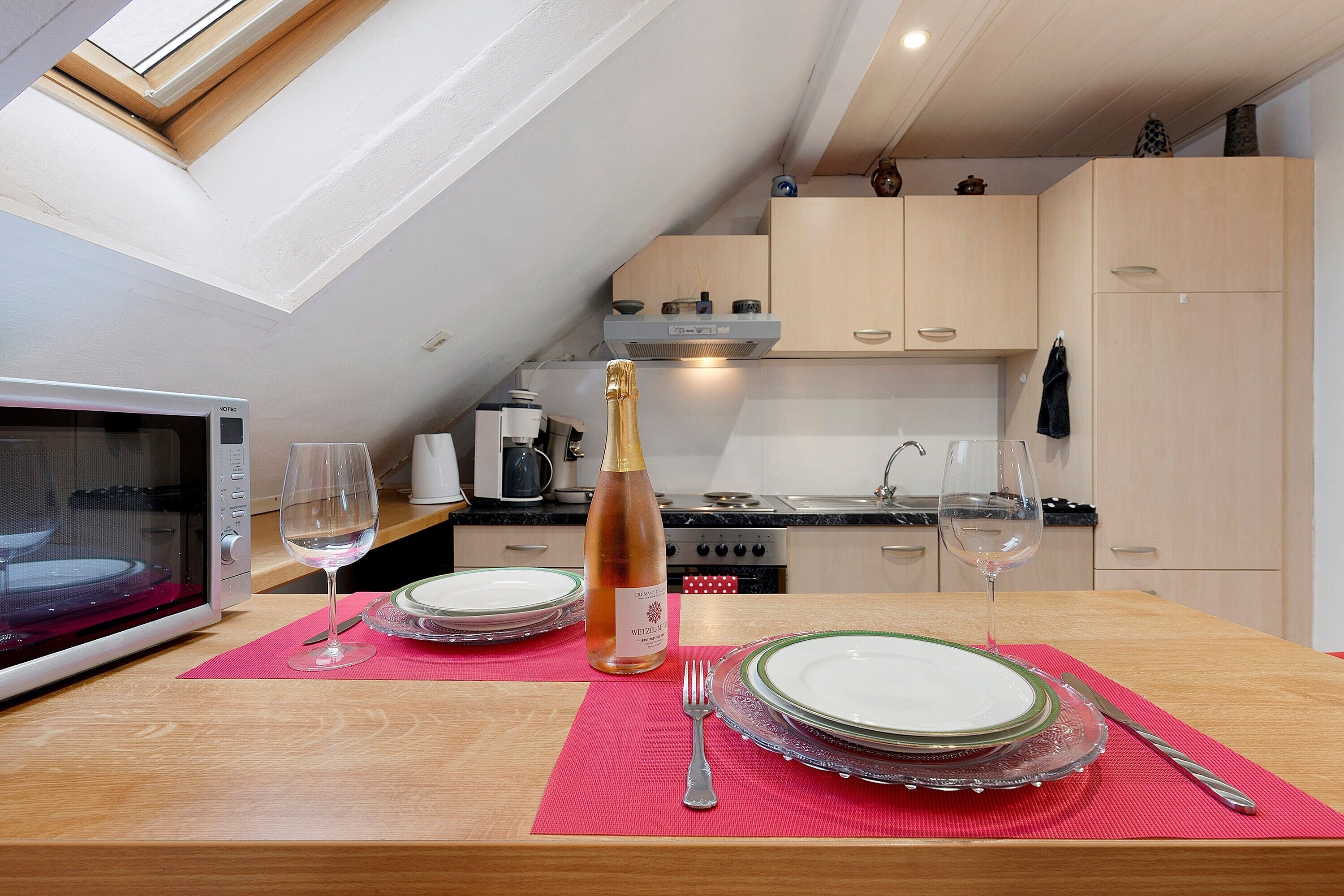 Una cocina con una mesa de comedor para dos, microondas y una botella de champán.