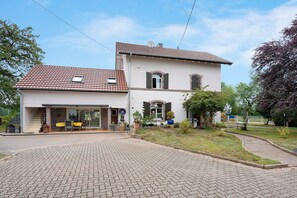 A two-story house with a paved driveway and a patio area with outdoor furniture.
