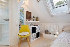 A bedroom with a bed, a yellow chair, a white dresser, and a window with a view of trees.