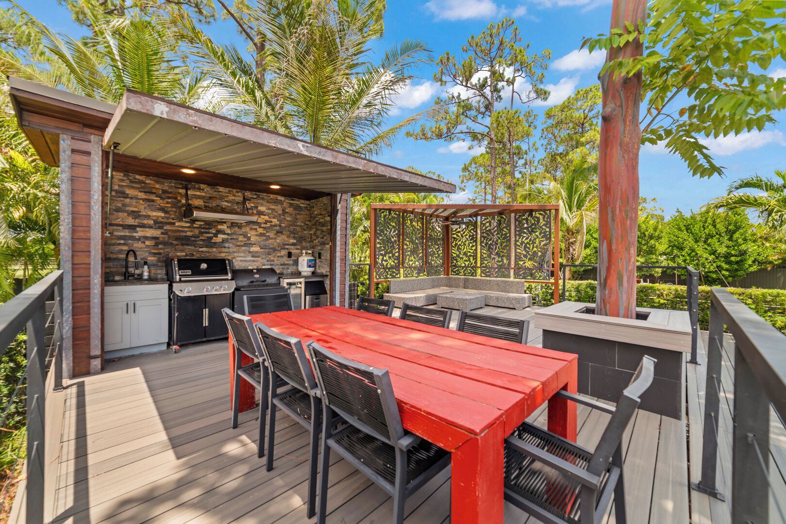An outdoor patio with a red table and chairs, a grill, and a stone wall.