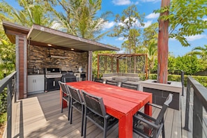 Une terrasse extérieure avec une table et des chaises rouges, un barbecue et un mur en pierre.