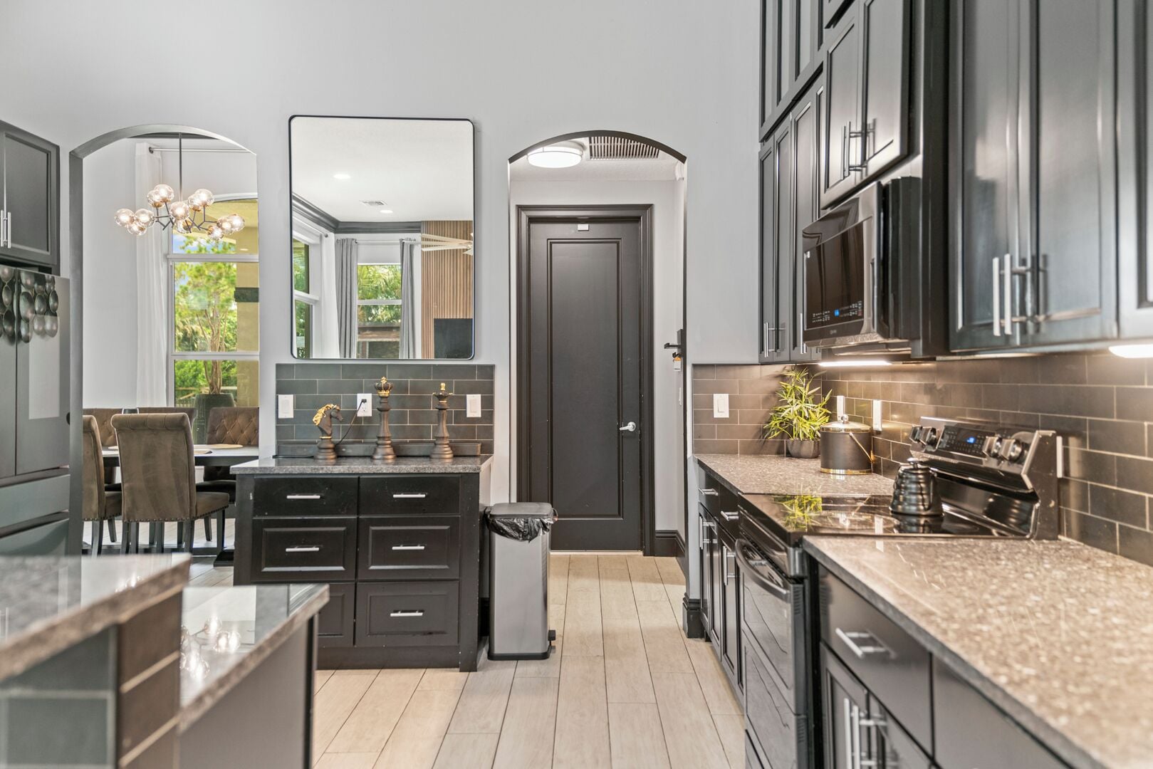A modern kitchen with dark cabinetry, a central island, and a dining area with a view.
