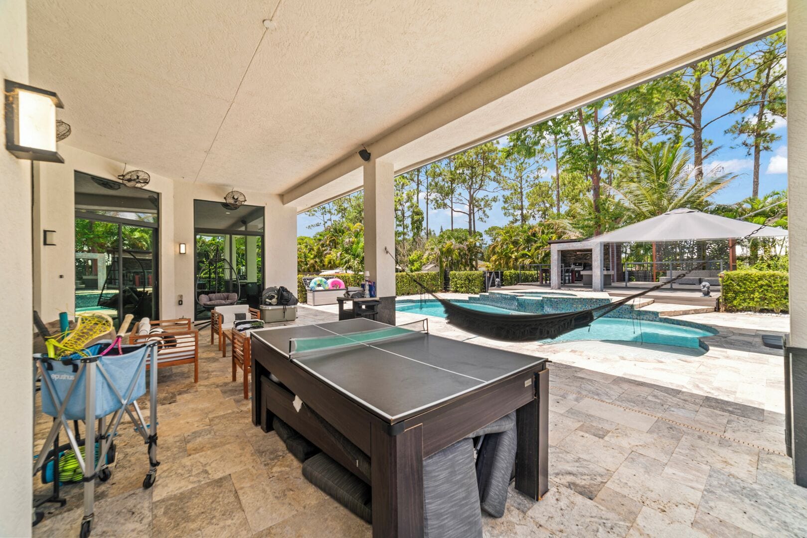 An outdoor recreational area with a ping pong table, seating, and a pool.