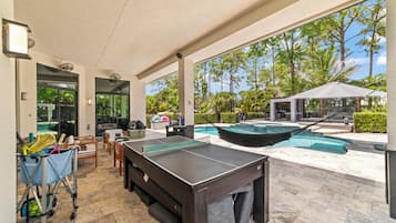 An outdoor recreational area with a ping pong table, seating, and a pool.
