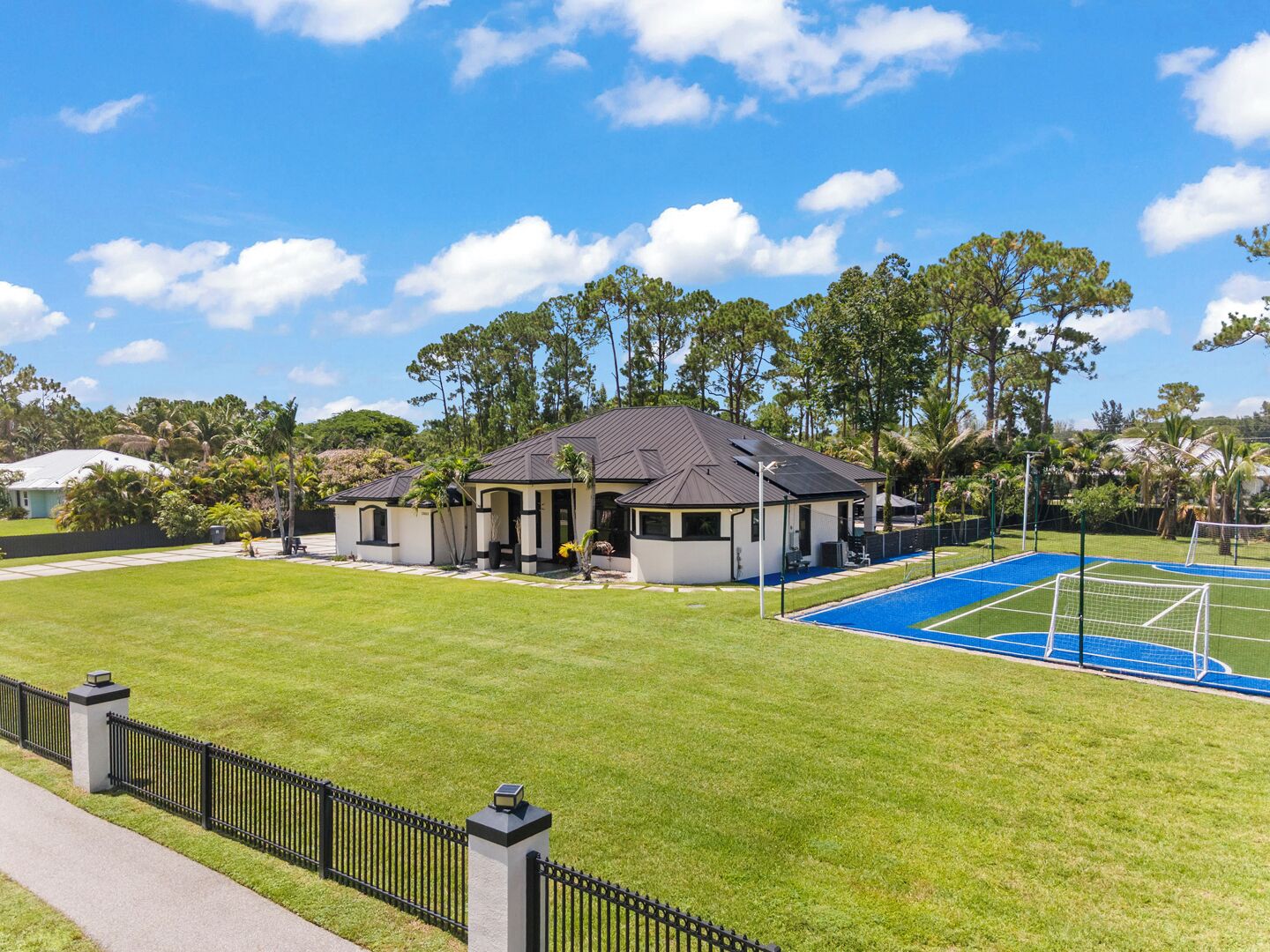 Propiedad residencial con cancha de tenis, patio cercado y una casa con techo oscuro.