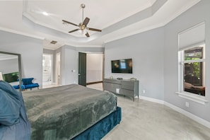 Une chambre à coucher comprenant un lit, une commode, un téléviseur et un ventilateur de plafond.