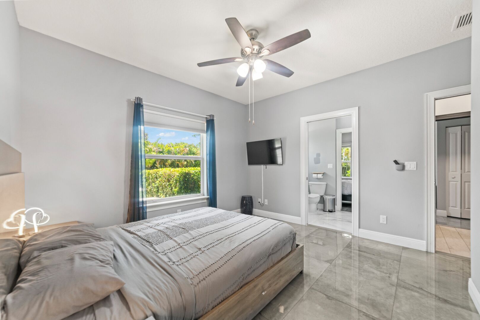 A bedroom with a bed, a ceiling fan, a TV, and a window with curtains.