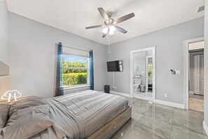 A bedroom with a bed, a ceiling fan, a TV, and a window with curtains.