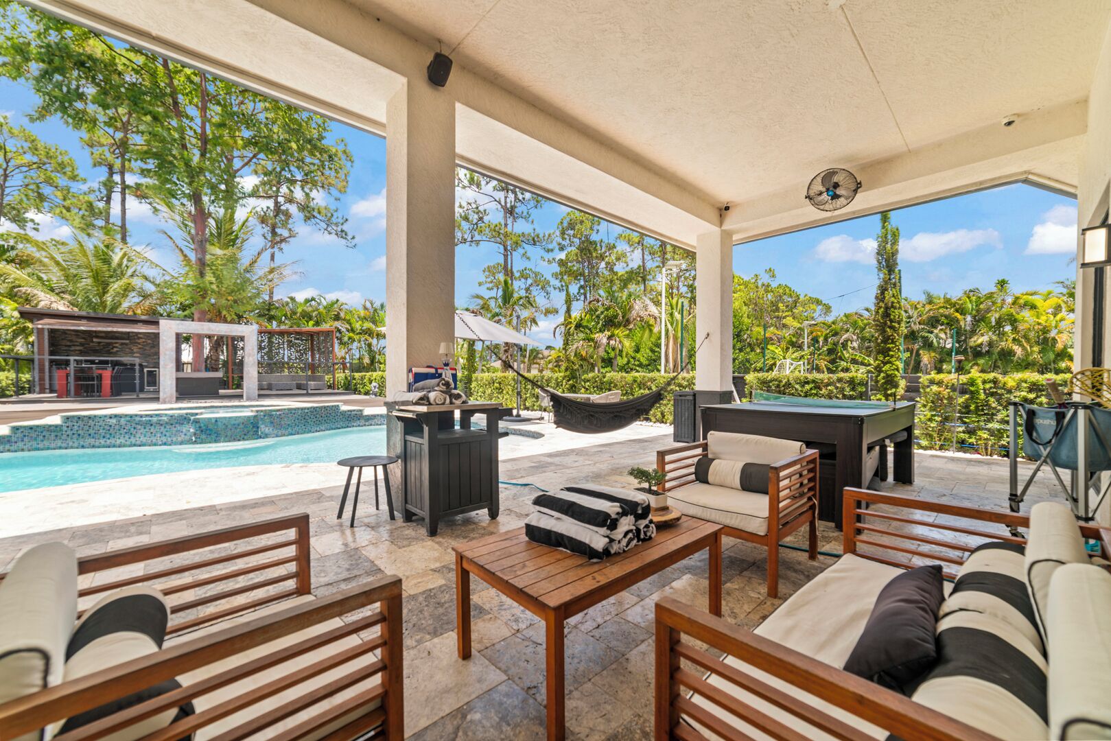 A covered outdoor area with a pool, lounge chairs, a table, and a hammock.