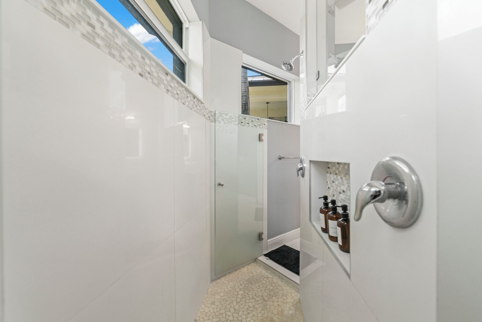 Un baño moderno con azulejos blancos, cabina de ducha de vidrio y tragaluz visible.
