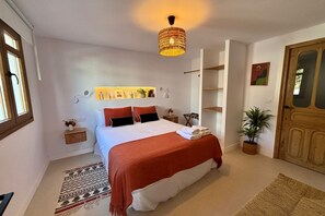 A bedroom with a bed, bedside tables, a hanging light fixture, a potted plant, and a door. - Ten Pool Apartment at Hacienda Clavero (Málaga)