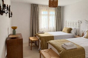 A hotel room with two beds, a wooden desk, a chair, a bedside table, and a window with curtains. - Hacienda Clavero Ten Pool Apartment (Málaga)