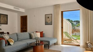 Una sala de estar moderna con un sofá seccional, una mesa de centro y vistas a un césped verde y edificios a través de un ventanal.