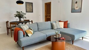 Una sala de estar con un sofá modular, una mesa redonda de centro, una mesa de comedor con sillas y obras de arte en las paredes.