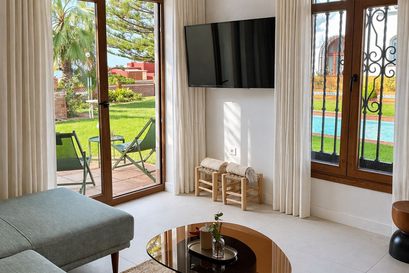 Uma sala de estar com sofá, televisão na parede e vista para uma piscina através de uma porta de vidro.