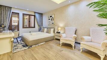 Une chambre d’hôtel avec un lit, deux fauteuils, un bureau et une grande fenêtre avec des rideaux.