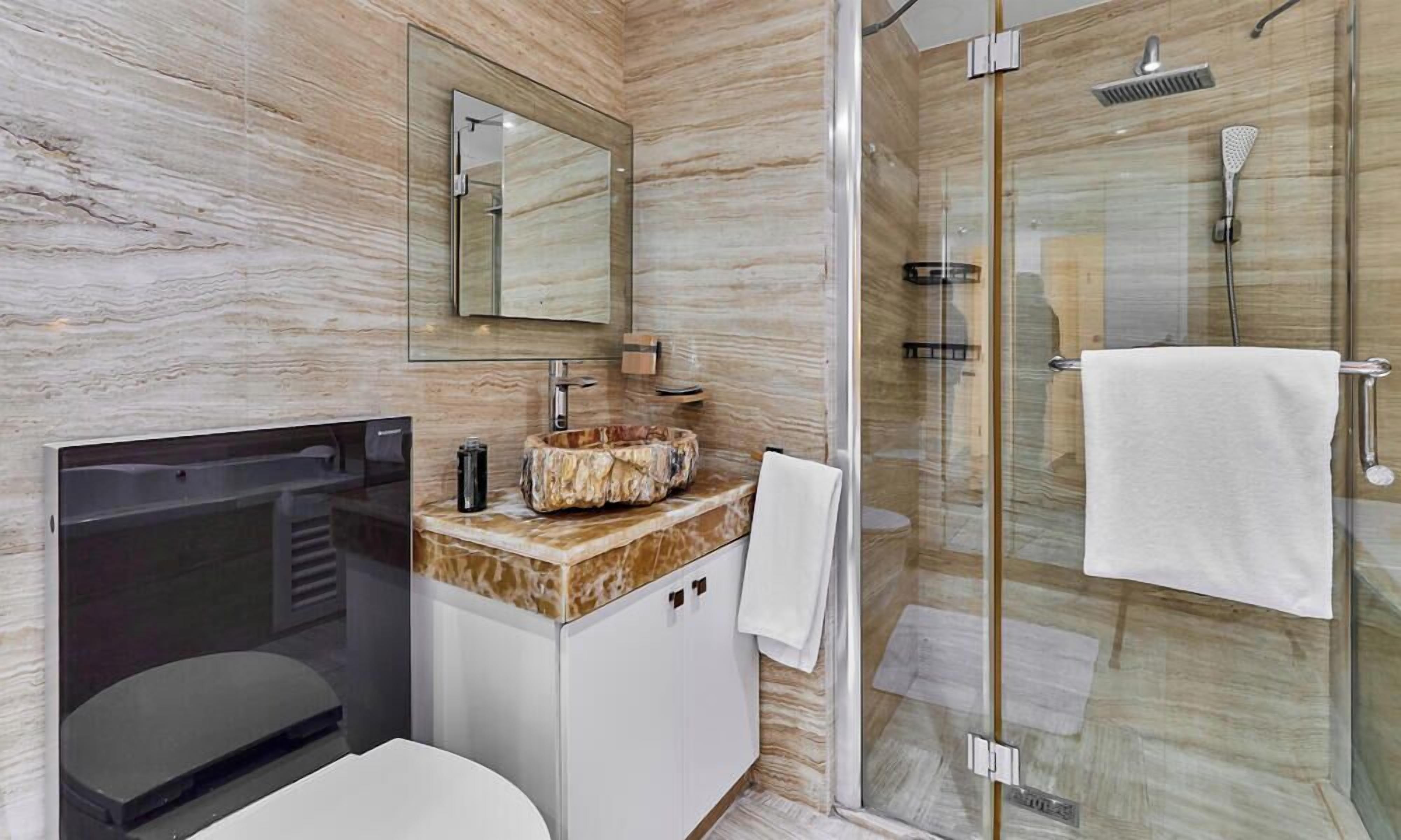 Une salle de bain moderne avec un meuble-lavabo en marbre, une cabine de douche en verre et des toilettes séparées.