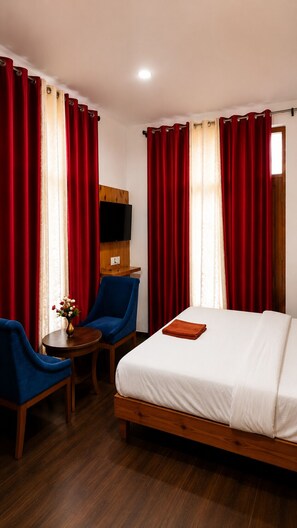 Habitación de hotel con una cama, dos sillones, una mesita con un florero y un televisor en la pared.