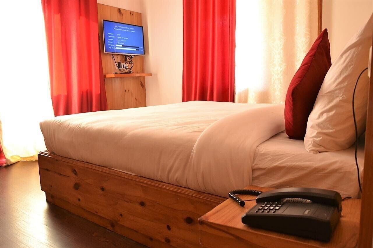 A bed with a wooden headboard, a television mounted on a wooden shelf, and a telephone on a wooden side table.