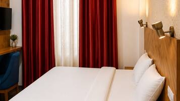 A hotel room with a wooden bed, a bedside telephone, and a desk with a chair.