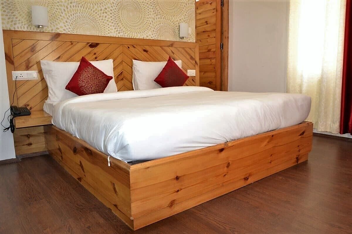 Una cama de madera con cabecera, ropa de cama blanca y dos almohadas rojas.