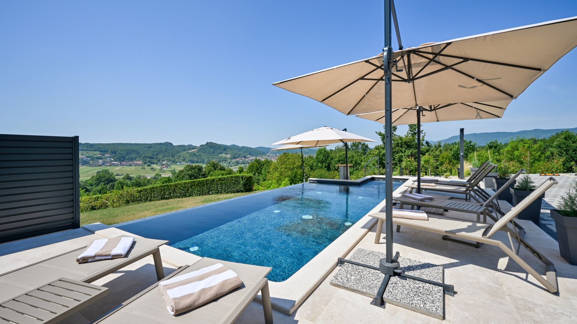 A rooftop infinity pool with lounge chairs and umbrellas, overlooking a scenic landscape.