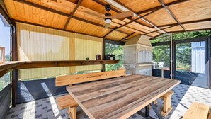 An outdoor patio with a wooden table and benches, a brick oven, and a ceiling fan. - Holiday Home Cerine Hill by Villas Guide (Gornji Vinkovec)
