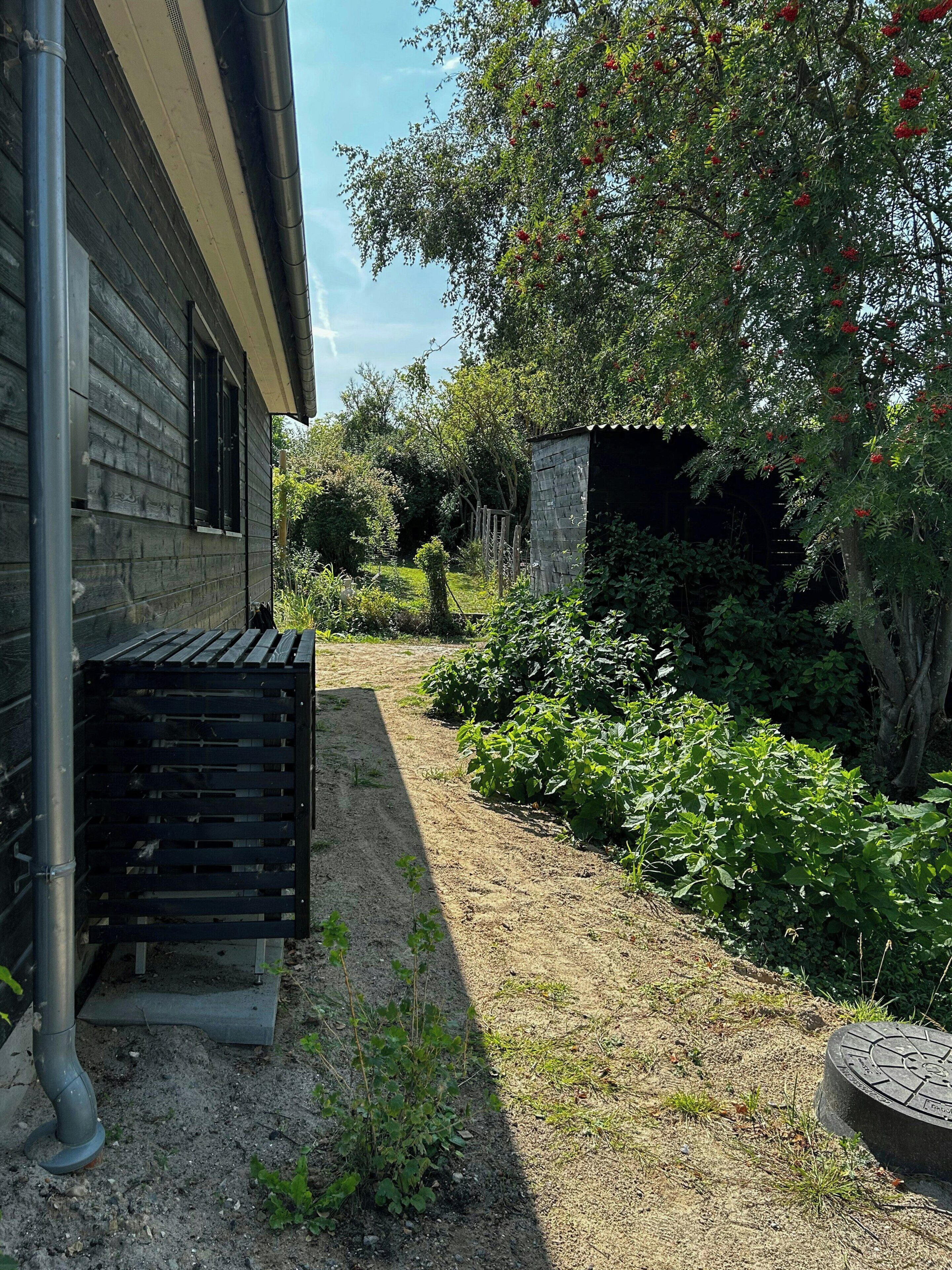 Een tuin met een houten huis, een metalen bank en een stenen constructie.