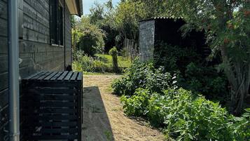 Een tuin met een houten huis, een metalen bank en een stenen constructie.
