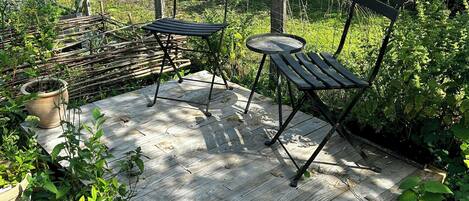 A wooden deck with outdoor furniture, surrounded by greenery and a house in the background.