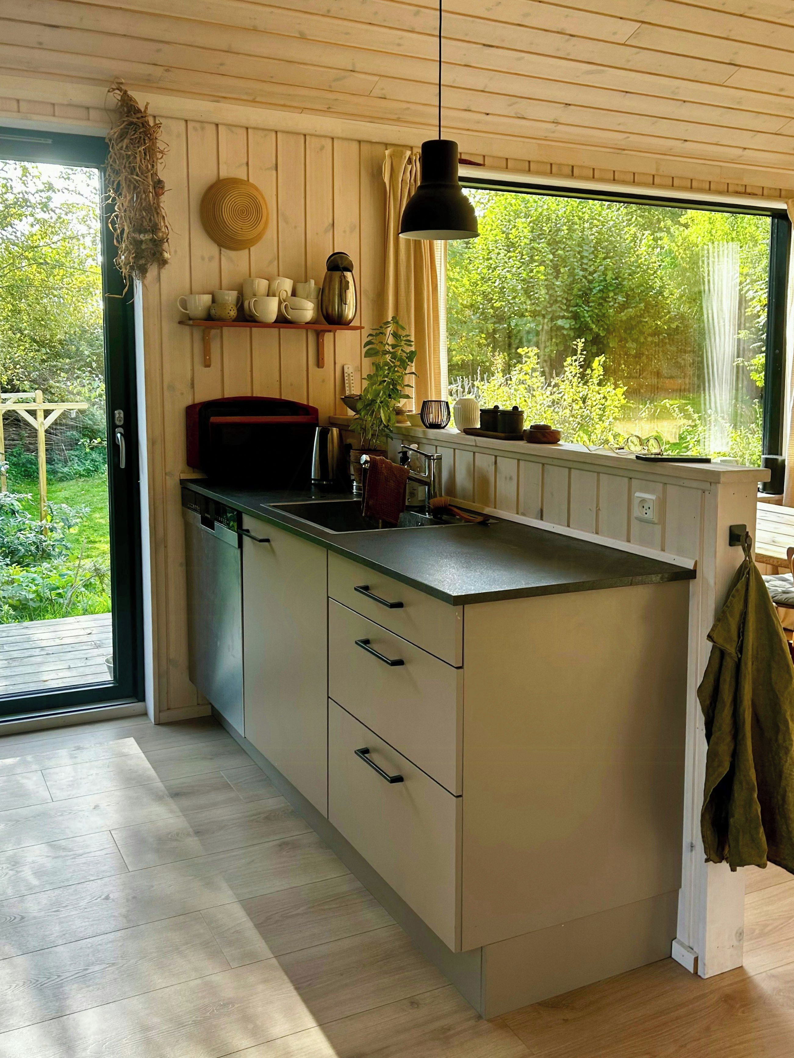Una cocina con techo de madera, ventana con vista a follaje y lámpara colgante.