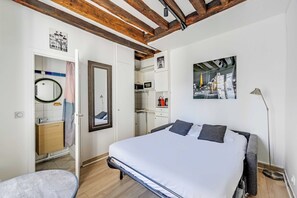 Ein Schlafzimmer mit Bett, Nachttisch, Lampe, Kleiderschrank und einem durch eine offene Tür einsehbaren Badezimmer.