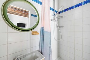 Ein Badezimmer mit weiß gefliesten Wänden, einem runden Spiegel, einer Dusche mit Duschbrause und einem hölzernen Waschtisch.