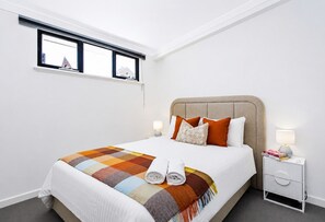 A hotel room with a bed, a nightstand, a lamp, and a window. - Historic Merchant's Quarters West End + Parking (Fremantle)
