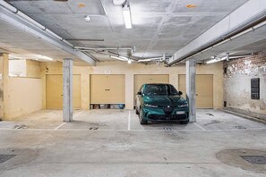 A parking garage with a green car parked in a spot, concrete pillars, and closed garage doors. - Historic Merchant's Quarters West End + Parking (Fremantle)