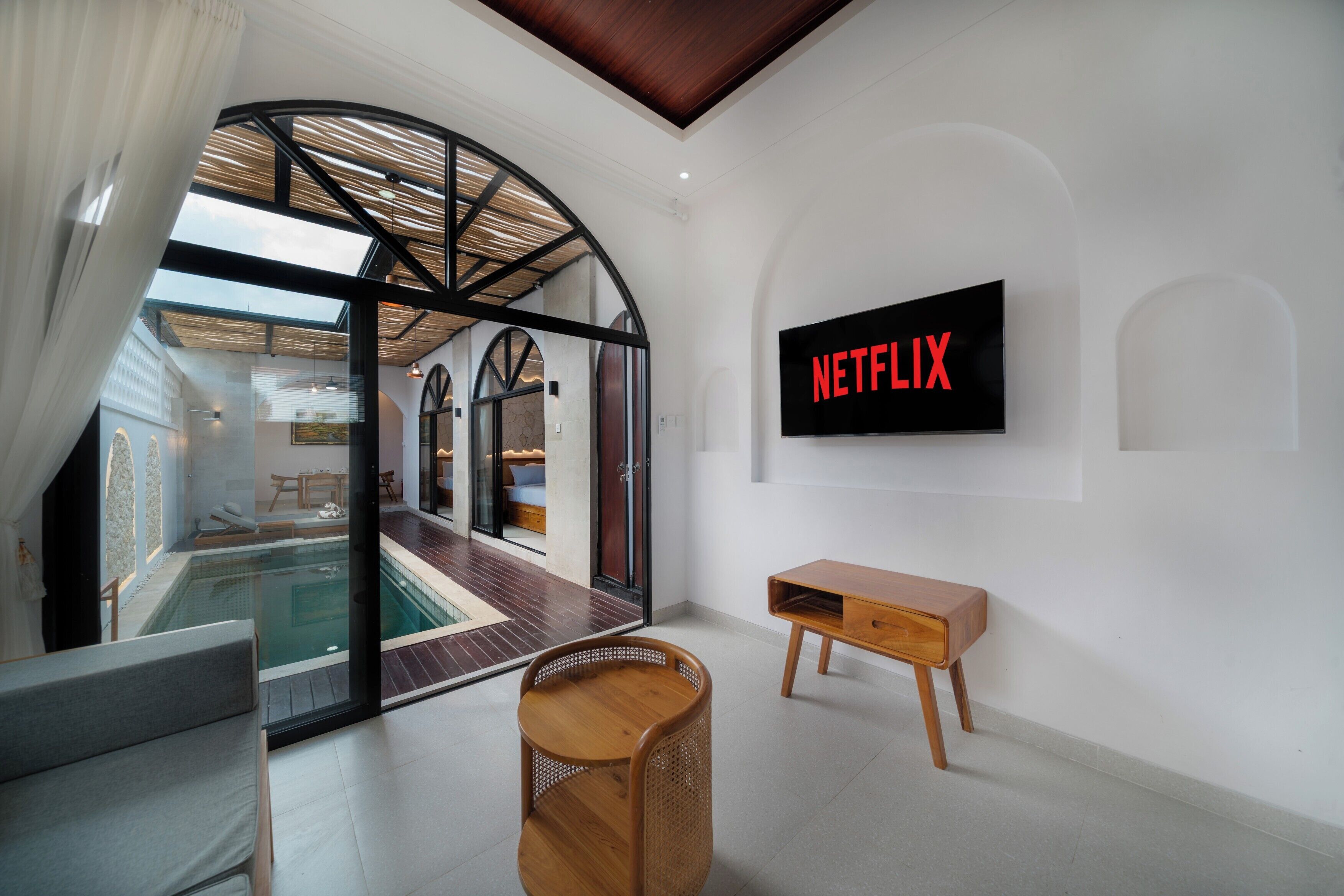 A modern interior with a glass-enclosed swimming pool, a wooden bench, and a wall-mounted television displaying the Netflix logo.