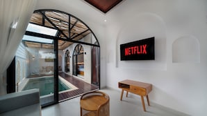 Um interior moderno com uma piscina envidraçada, um banco de madeira e uma televisão na parede exibindo o logotipo da Netflix.