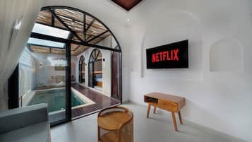 A modern interior with a glass-enclosed swimming pool, a wooden bench, and a wall-mounted television displaying the Netflix logo.