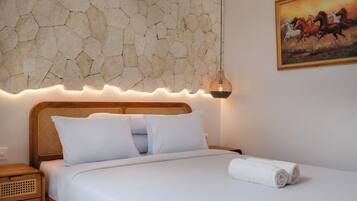 A bed with white linens, a stone wall, a painting of horses, and a bedside lamp.