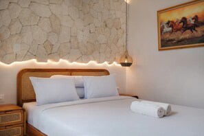 Een bed met witte lakens, een stenen muur, een schilderij van paarden en een bedlamp.