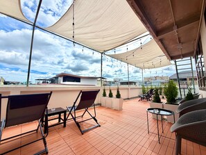 En udendørs terrasse med et bord og stole, et markise og udsigt over bybilledet.