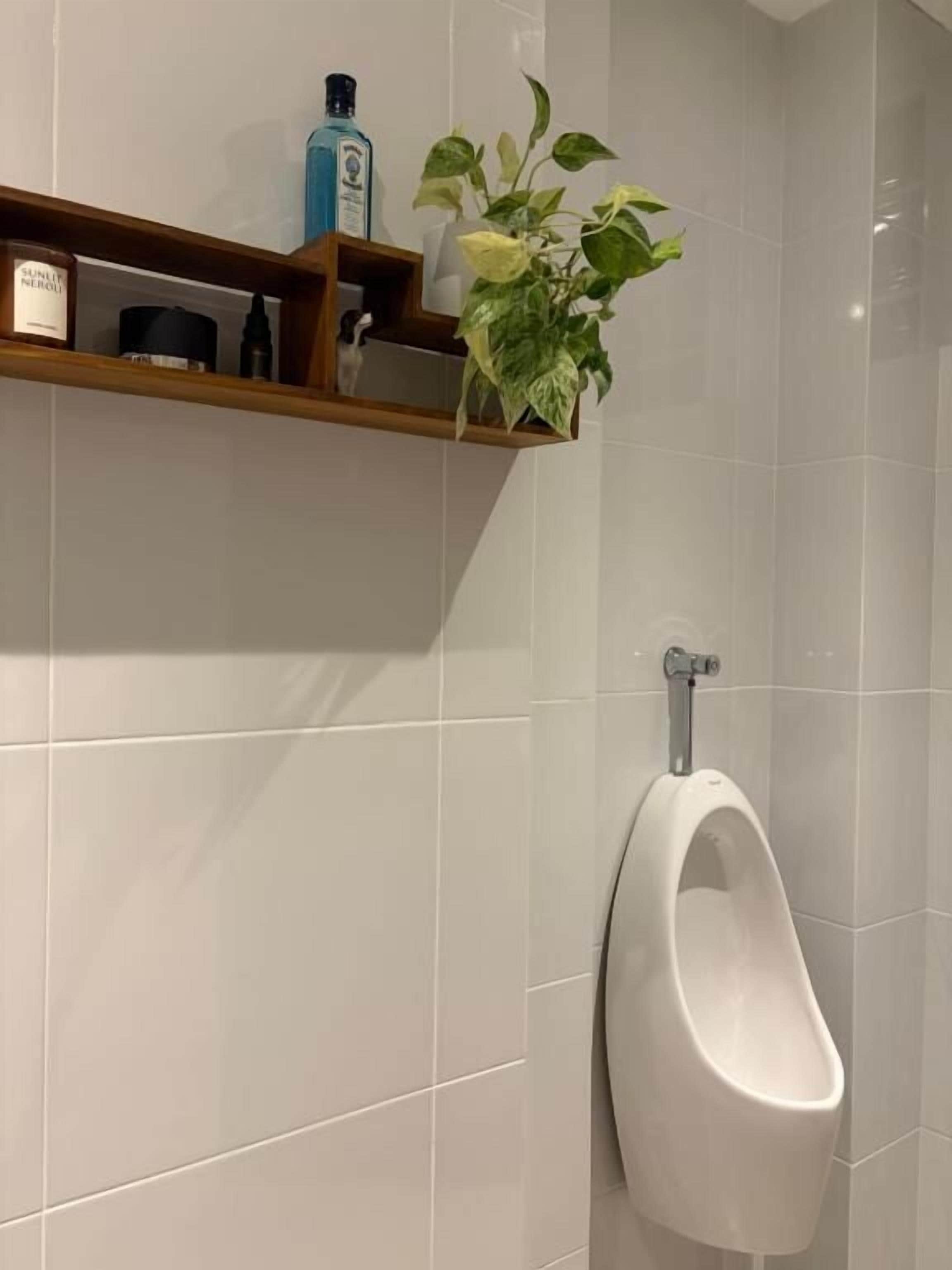 A urinal in a bathroom with a shelf above it holding toiletries and a potted plant.