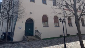 Ein weißes Gebäude mit zahlreichen Fenstern und einer grünen Tür, ausgestattet mit einem courtyard aus Steinplatten und einigen Bäumen.
