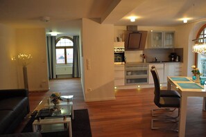 A modern kitchen with stainless steel appliances, a dining area with a glass table, and a living room with a dark sofa and a glass coffee table. - Vacation Rental: 65 square meters, separate bedroom and balcony, Apt. 7 (Aschau im Chiemgau)