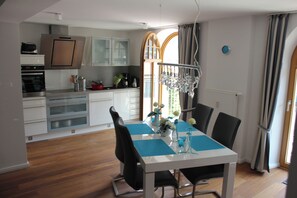 A modern kitchen with white cabinets, a dining table with blue placemats, and a chandelier. - Vacation Rental: 65 square meters, separate bedroom and balcony, Apt. 7 (Aschau im Chiemgau)