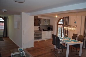 A modern kitchen with white cabinets, a dining area with a table and chairs, and a chandelier. - Vacation Rental: 65 square meters, separate bedroom and balcony, Apt. 7 (Aschau im Chiemgau)