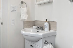 A bathroom with a white sink, a towel ring, a mirror, and a bottle of hand soap. - Edmonton Convention Centre Studio | Parking, Wifi (Edmonton)