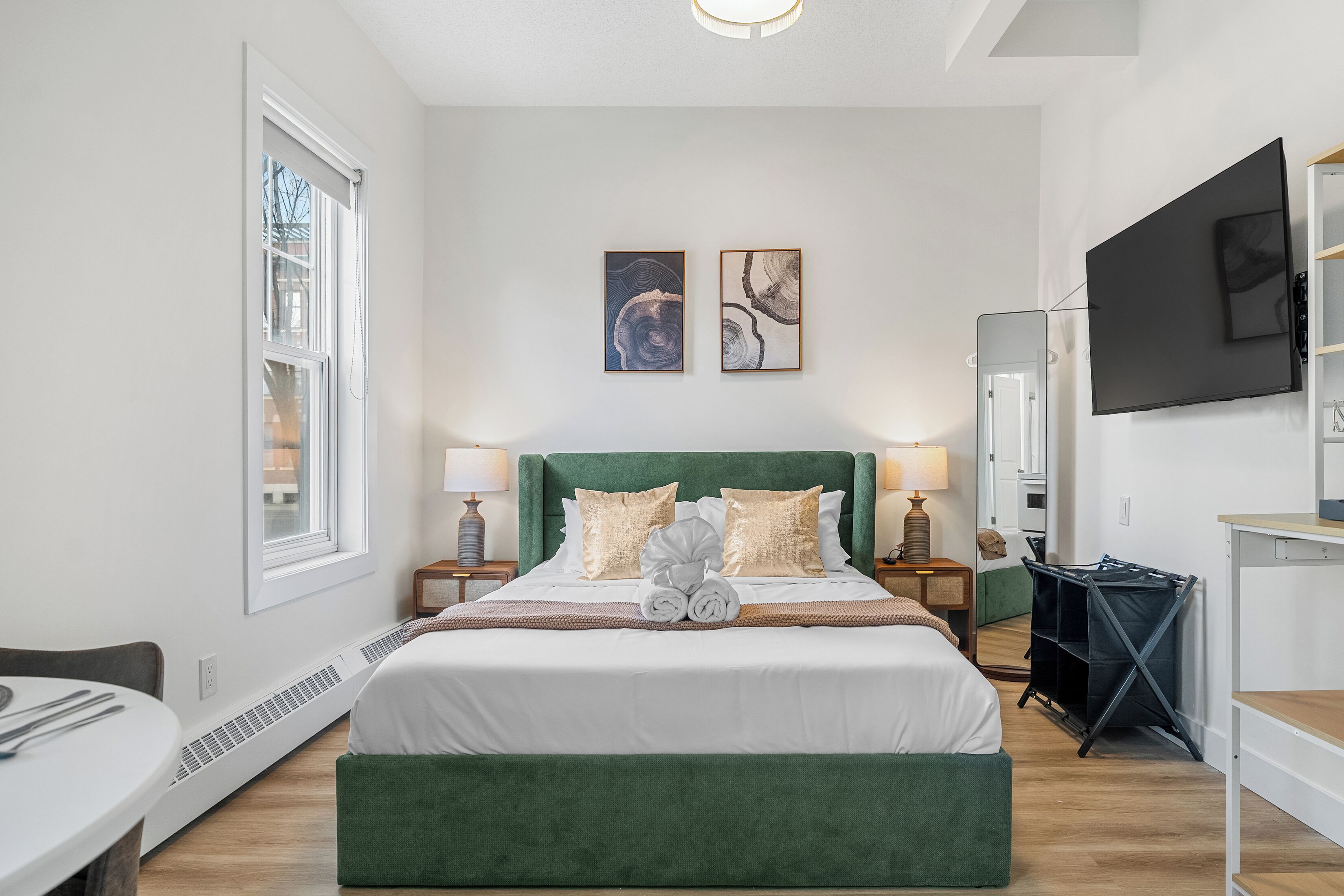 A modern hotel room with a large bed, two bedside tables, a flat-screen TV, and artwork on the wall.