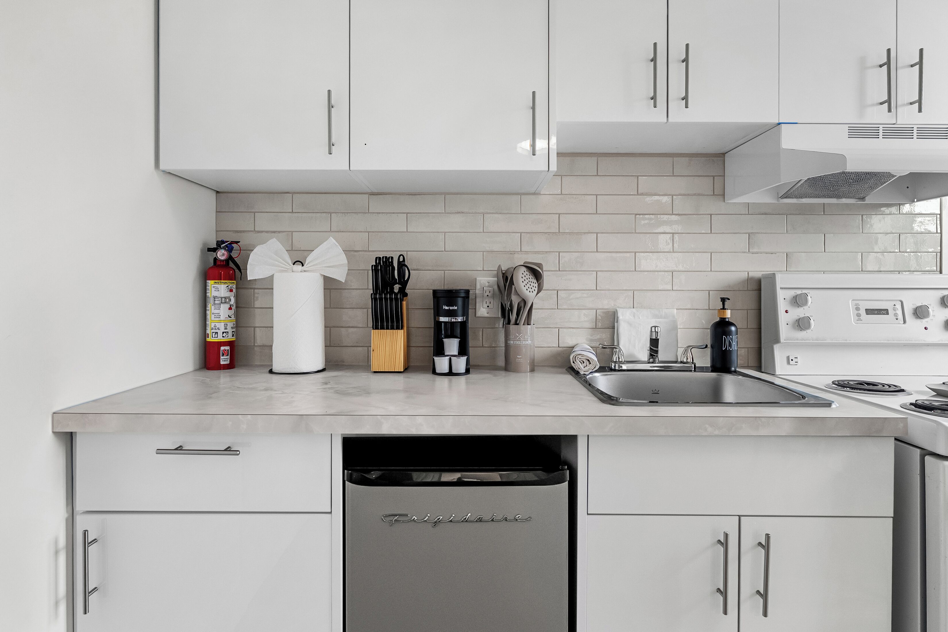 A modern kitchen with white cabinets, a dishwasher, a sink, and a stove.